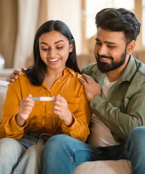excited-indian-couple-holding-positive-pregnancy-test-while-sitting-couch-home-loving-husband_116547-78629