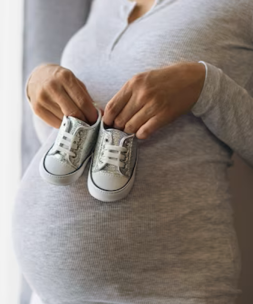 pregnant-woman-gray-jacket-holds-baby-shoes